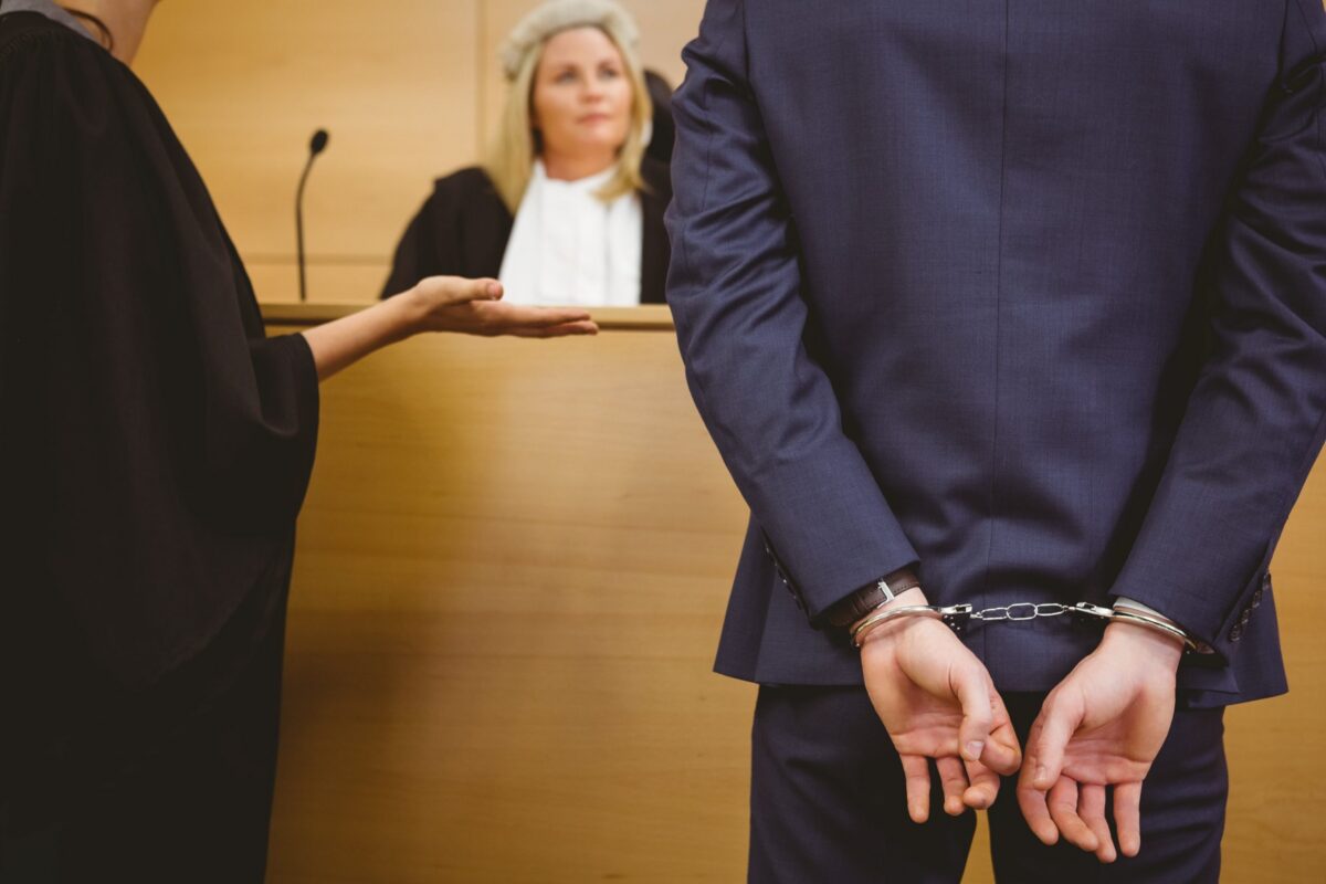 Guy in a suit with handcuffs before a judge